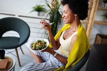 Fotobehang Kruidenier Beautiful afro american woman eating vegetable salad at home.  © NDABCREATIVITY