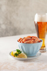 Boiled shrimp prawns in a shell with lemon and parsley in a bowl on a light background.