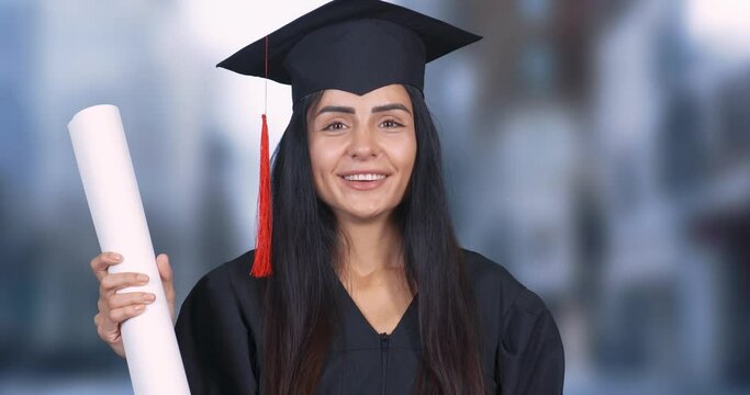 Young student female in a robe and hat holds a diploma paper scroll in his hands, a beautiful girl smiles and looks at the camera, woman in graduation robe.