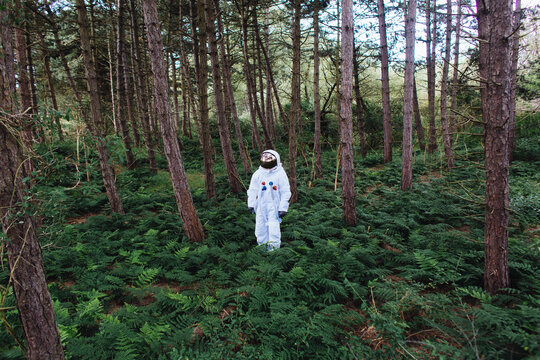 Man in space suit standing in a forest.