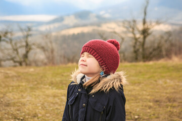 a little girl in a hat stands high in the mountains with her eyes closed. travel in winter with...