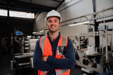 Male engineer standing smiling with crossed arms in factory 