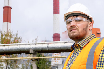 A man in a construction helmet against the backdrop of a large plant.
