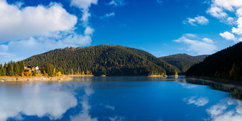 panorama of mountain lake in autumn season. beautiful countryside scenery on a sunny morning. bright blue sky with fluffy clouds reflecting on the water surface