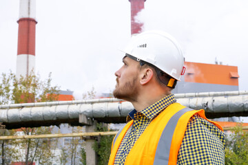 A man in a construction helmet against the backdrop of a large plant.