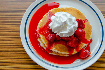 Pancakes with strawberries, cream and syrup on a plate. Top view. 