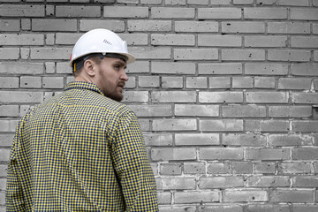 Builder in a hard hat on a brick wall background.