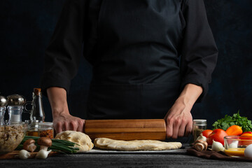 The chef in black with wooden rolling pin baking dough isolated on black background. Cooking pie. Traditional healthy food.