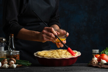 The chef in black apron smearing the pie be the eggs. The girl's hand with culinary brash. Professional kitchen. Restaurant concept. Preparing healthy food.