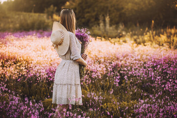 Young woman with a bouquet of wildflowers standing on a sunny blooming meadow