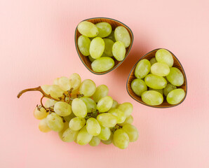 Green grapes in bowls on a pink background. flat lay.