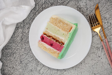 A piece of layered cake with berries and pistachio on a plate. Top View