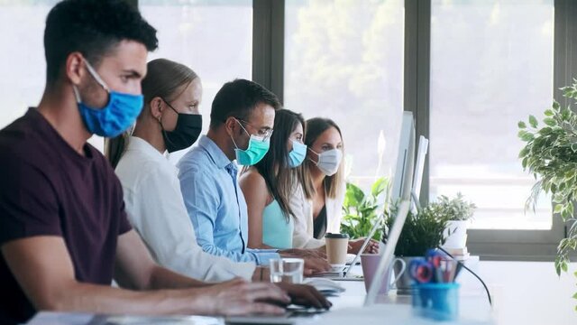 Video of successful concentrated business team wearing a hygienic facial mask while working together in the office keeping safe distances on coworking place.