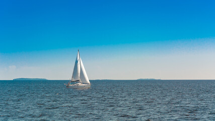 Naklejka na ściany i meble A lonely white sailing yacht sails in the open sea. Sunny day. Calm water surface