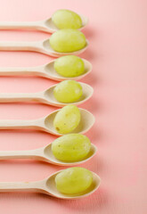 Green grapes in wooden spoons on a pink background. high angle view.