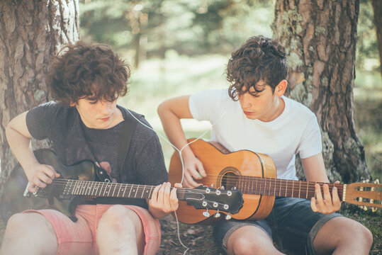 Two teenagers listening to music sharing their headphones while playing the guitar.