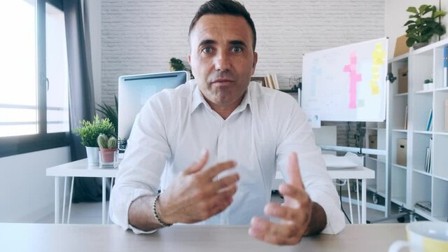 Video of smart mature business man looking and speaking through the webcam while making a video conference from the office.