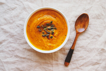 Hot pumpkin soup served with squash seeds in a bowl on wooden background.