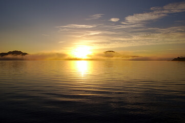 Fototapeta na wymiar 湖面に雲の漂う早朝の湖に昇る朝日