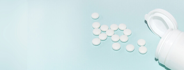 White open plastic jar with a bunch of white scattered pills on a light blue background, medicine concept, copy of the space, banner
