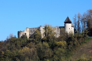 Abandoned old stone medieval town castle with two partially renovated guard towers on top of small hill surrounded with dense forest on clear blue sky background