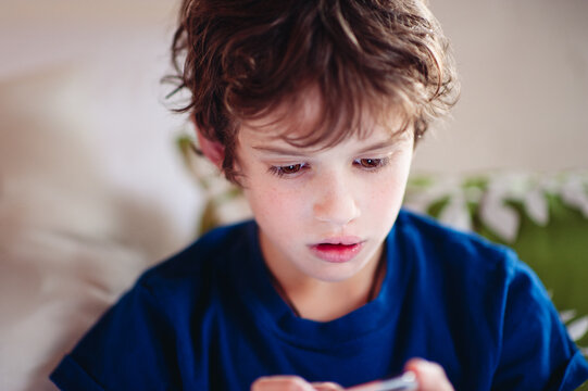 Boy in pyjamas sits on a bed playing with an electronic game