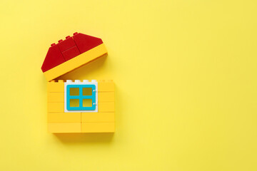 Plastic building blocks on yellow background. Yellow unfinished house on yellow background. Mortgage symbol, top view, copy space.