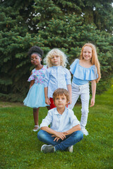 Fototapeta premium Playing. Interracial group of kids, girls and boys playing together at the park in summer day. Friendship has no race. Happiness, childhood, education, diversity concept. Look happy and sincere.