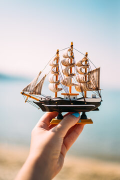 Person holding small ship toy in front of the sea