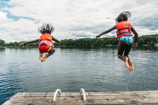 Two African-American Girls in Life Vests Jumping In A Lake