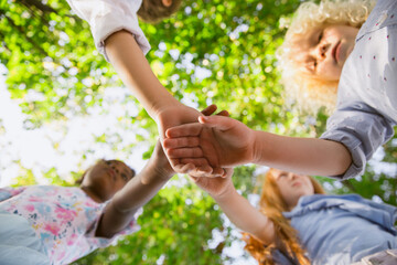 Fototapeta premium Dream team. Interracial group of kids, girls and boys playing together at the park in summer day. Friendship has no race. Happiness, childhood, education, diversity concept. Look happy and sincere.