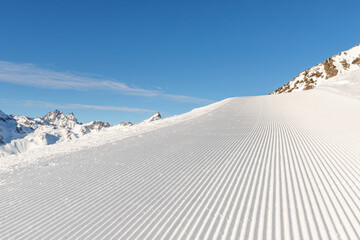Close-up straight line rows of freshly prepared groomed ski slope piste with bright shining sun and...
