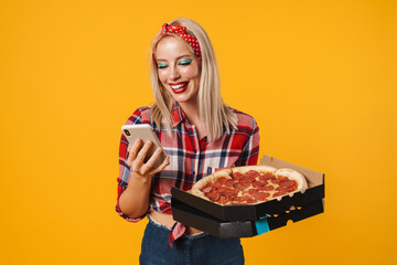 Image of joyful charming pinup girl using cellphone while holding pizza