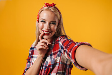 Image of cheerful beautiful pinup girl smiling while taking selfie photo