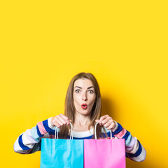 Young woman in sweater holds shopping bags with purchases on yellow background