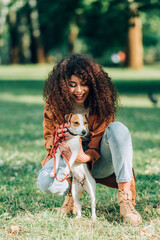 Selective focus of woman in raincoat petting jack russell terrier in park
