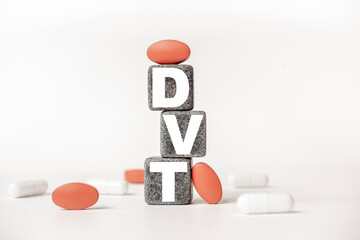 a group of white and red pills and cubes with the word DVT Deep venous thrombosis on them, white background. Concept carehealth, treatment, therapy.