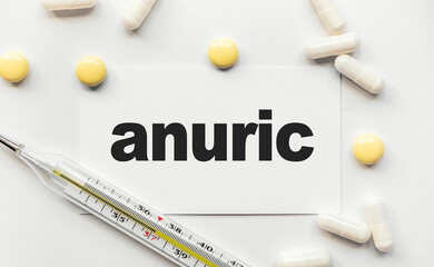 On the white business card the inscription Anuric Not producing urine in black letters. Nearby tablets and capsules lie.ac Medical concept. Disease, treatment and prevention