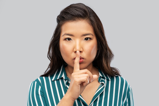 silence, confidentiality and people concept - portrait of young asian woman making hush gesture over grey background