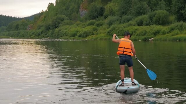 A man with a paddle in a life jacket floats on a sup surf on a river