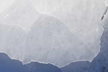 Close-up of cracked ice on a frozen lake in the winter, viewed from above. Abstract textured full frame background. Copy space, top view.