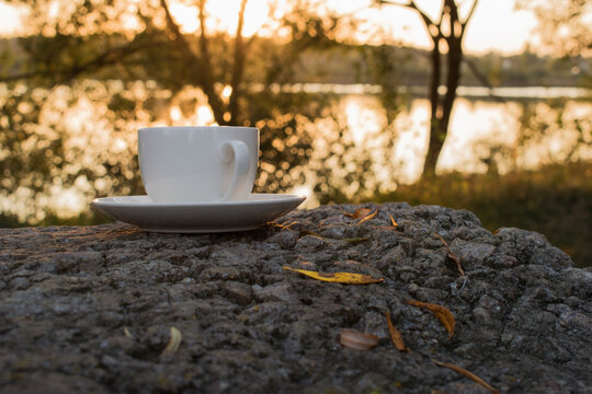 A white Cup and saucer stands on a stone with autumn leaves on a blurred background of nature in the form of a bokeh. The concept of the ability to devote time to yourself rest and relaxation