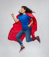 women's power and people concept - happy asian woman in red superhero cape jumping over grey...