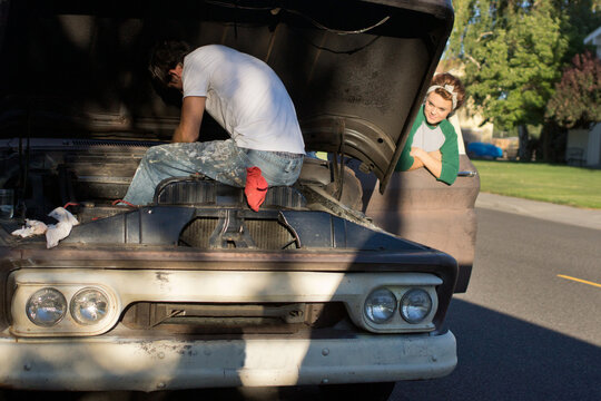 Young man sits in motor compartment repairing engine