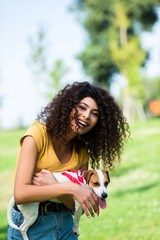 Fototapeta na wymiar curly woman looking at camera and laughing while holding jack russell terrier dog