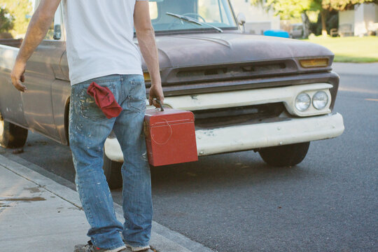 Young man carries toolbox by an old pickup