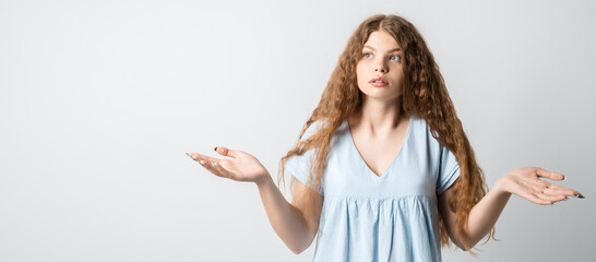 Pretty girl looking at camera shrugging shoulders over white background. Concept of doubt,...