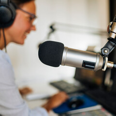 Microphone in a podcasting studio, host and the broadcasting equipment in the background