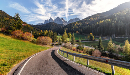 Fototapeta premium Amazing mountain landscape at autumn sunny day. scenic alpine scenery of Dolomites Alps. Wonderful view on Mountain valley, forest, and asphalt road for majestic rocky peak. Santa Maddalena. Italy