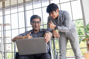 A middle-aged Asian father sits in a wheelchair and has a son next to him chatting on video calls on a laptop.